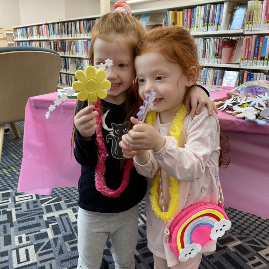 Two children with red hair hold up wands they made at Main Branch.