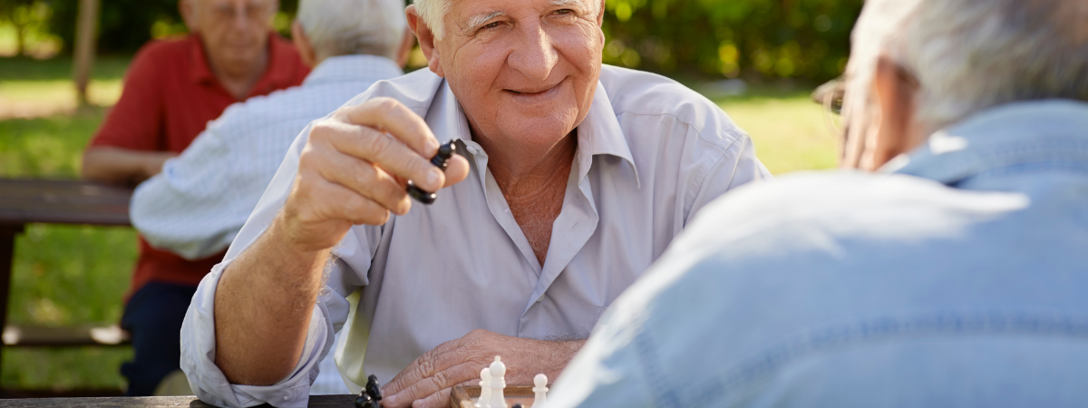 People sitting at a table in a park playing chess.