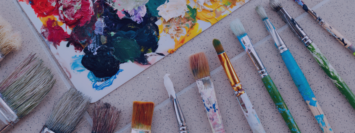 A palette with paint and paint brushes on a tile floor.