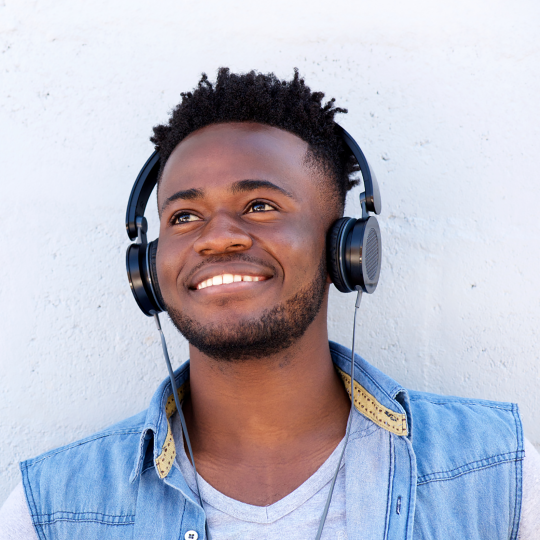 A Black man wearing headphones and smiling at something off camera. 