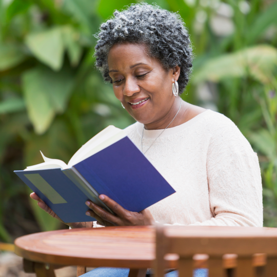 An older Black woman reading outside at a table. 